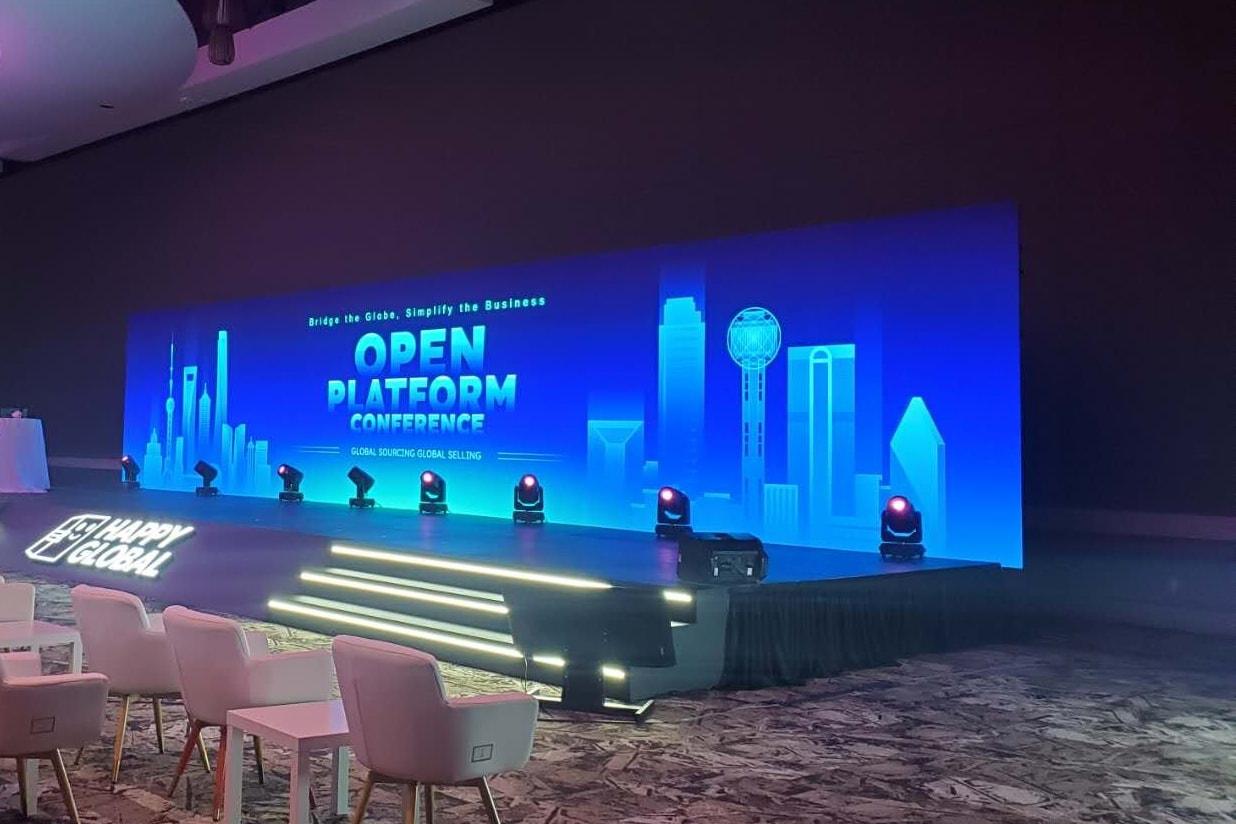 A row of moving-head lights along a stage lip in front of a long LED wall