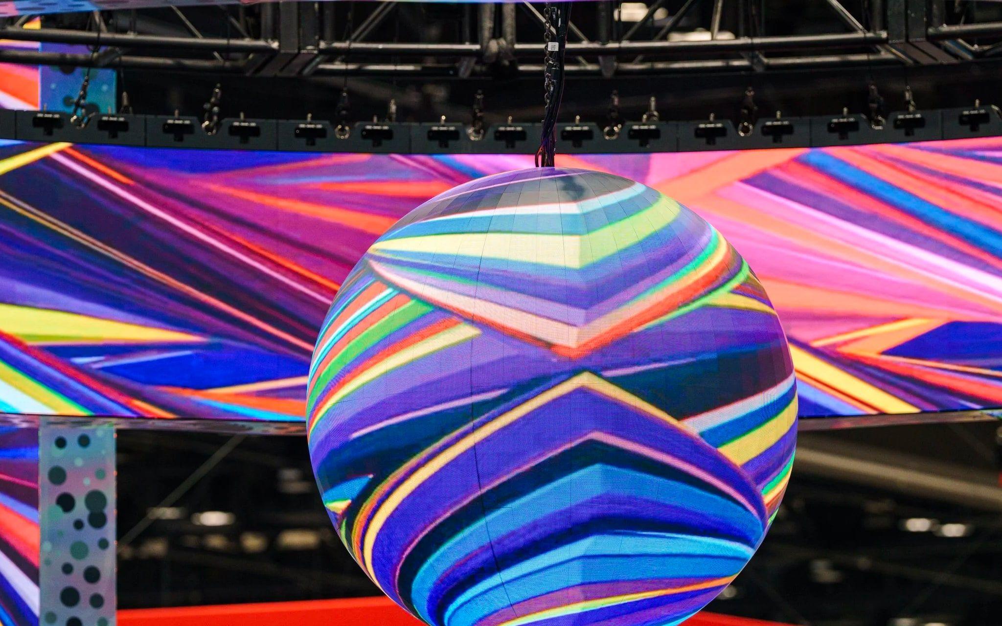 A hanging LED sphere in front of a curved LED ring, both playing bright striped color