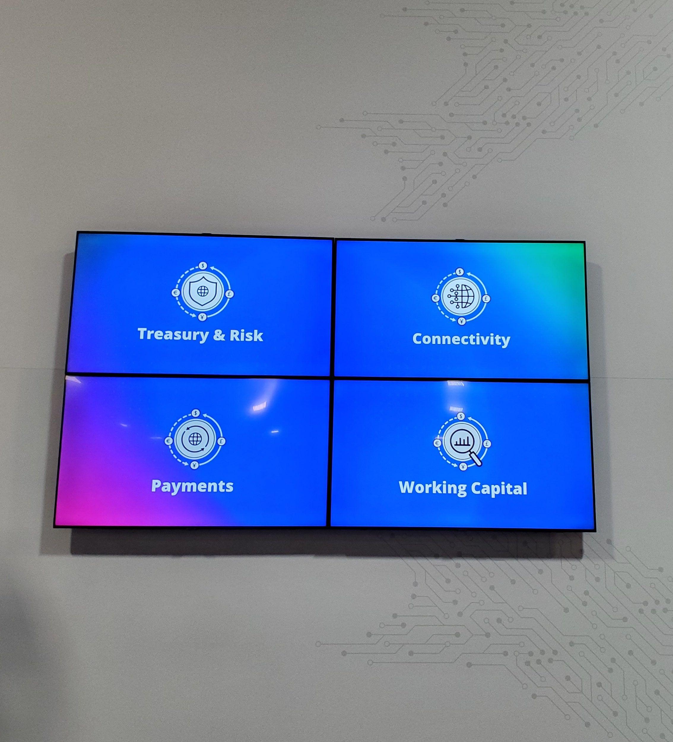 Four flat-panel TVs mounted as a 2 x 2 video wall on a white trade show booth wall